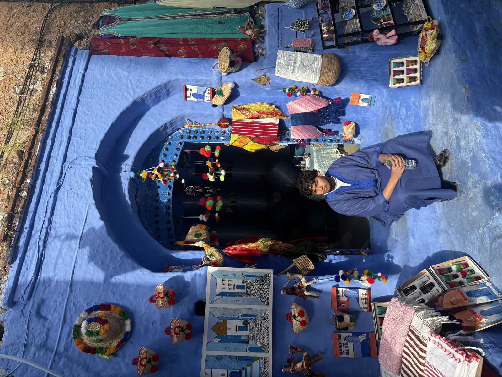 Fahmid seated outside a blue-painted shop with colourful crafts